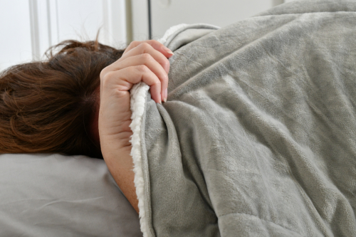 Image of individual pulling the covers back over their head in bed